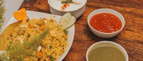 A plate of biryani with side dishes of raita and chutney on a wooden table.