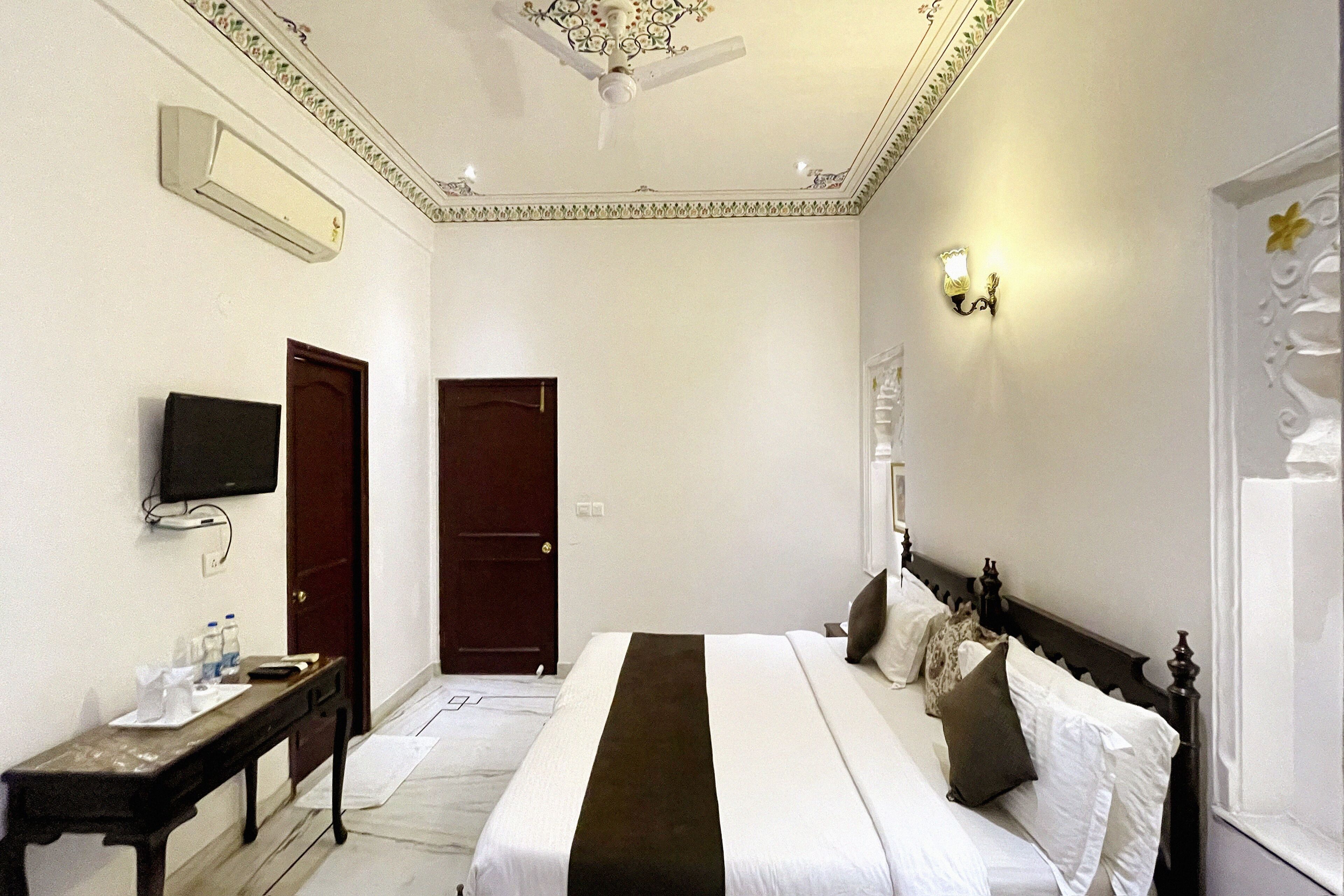 Una habitación de hotel con cama, escritorio, televisor y puerta.