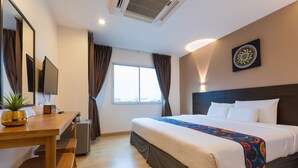 Ein Hotelzimmer mit Bett, Schreibtisch mit Stuhl, kleinem Tisch, Topfpflanze, Flachbildfernseher und einem Fenster mit Vorhängen.