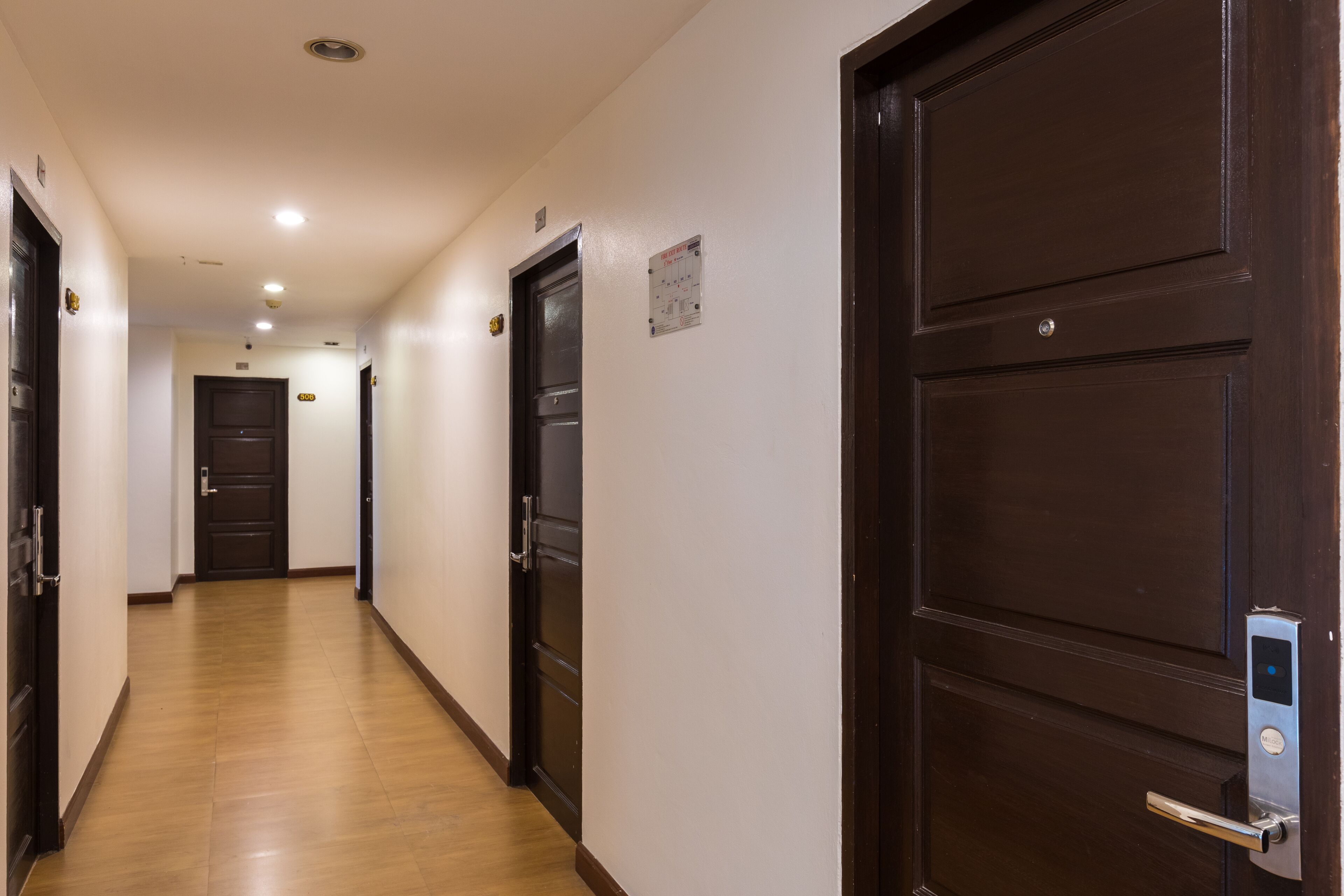 Un pasillo con piso de madera, puertas de madera oscura y una pared de color claro.