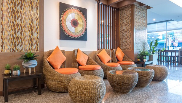 Eine Lobby mit Korbstühlen, orangefarbenen Kissen, einer Mosaikwand und einem großen abstrakten Gemälde.