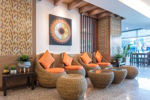Un hall d’entrée avec des fauteuils en osier, des coussins orange, un mur décoré de mosaïques et un grand tableau abstrait.