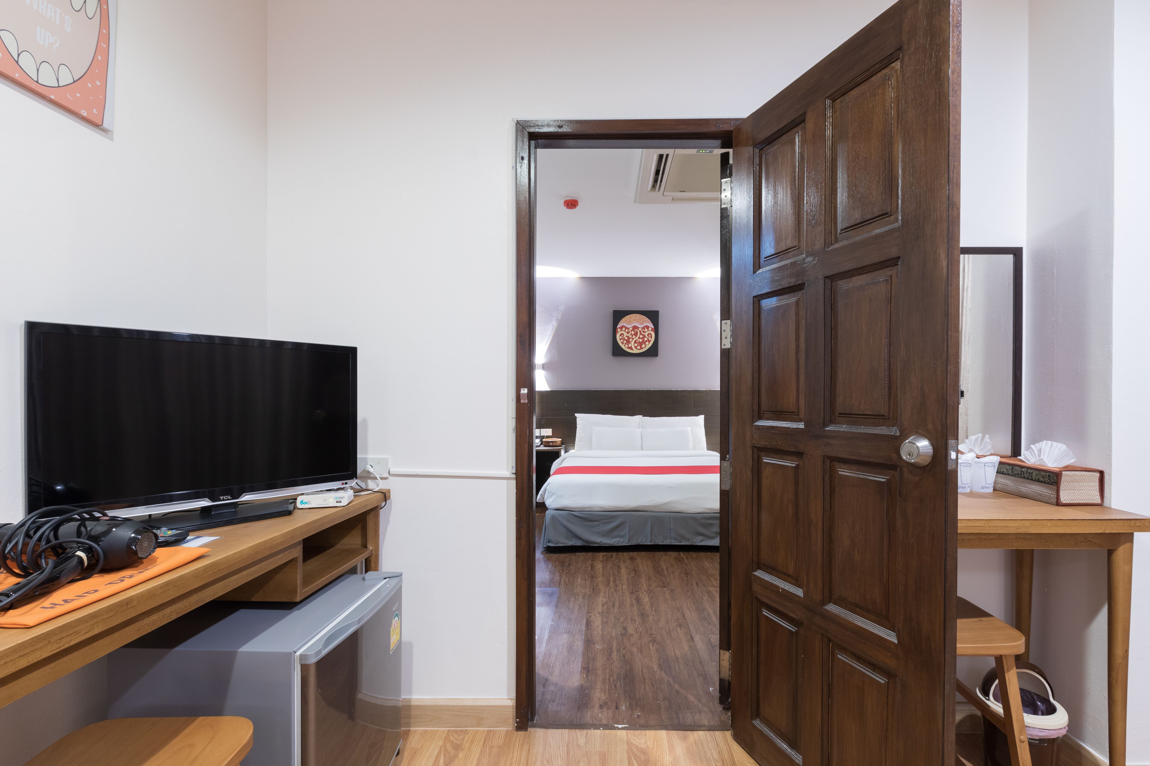 Habitación de hotel con un escritorio de madera, televisor y cama con ropa blanca.