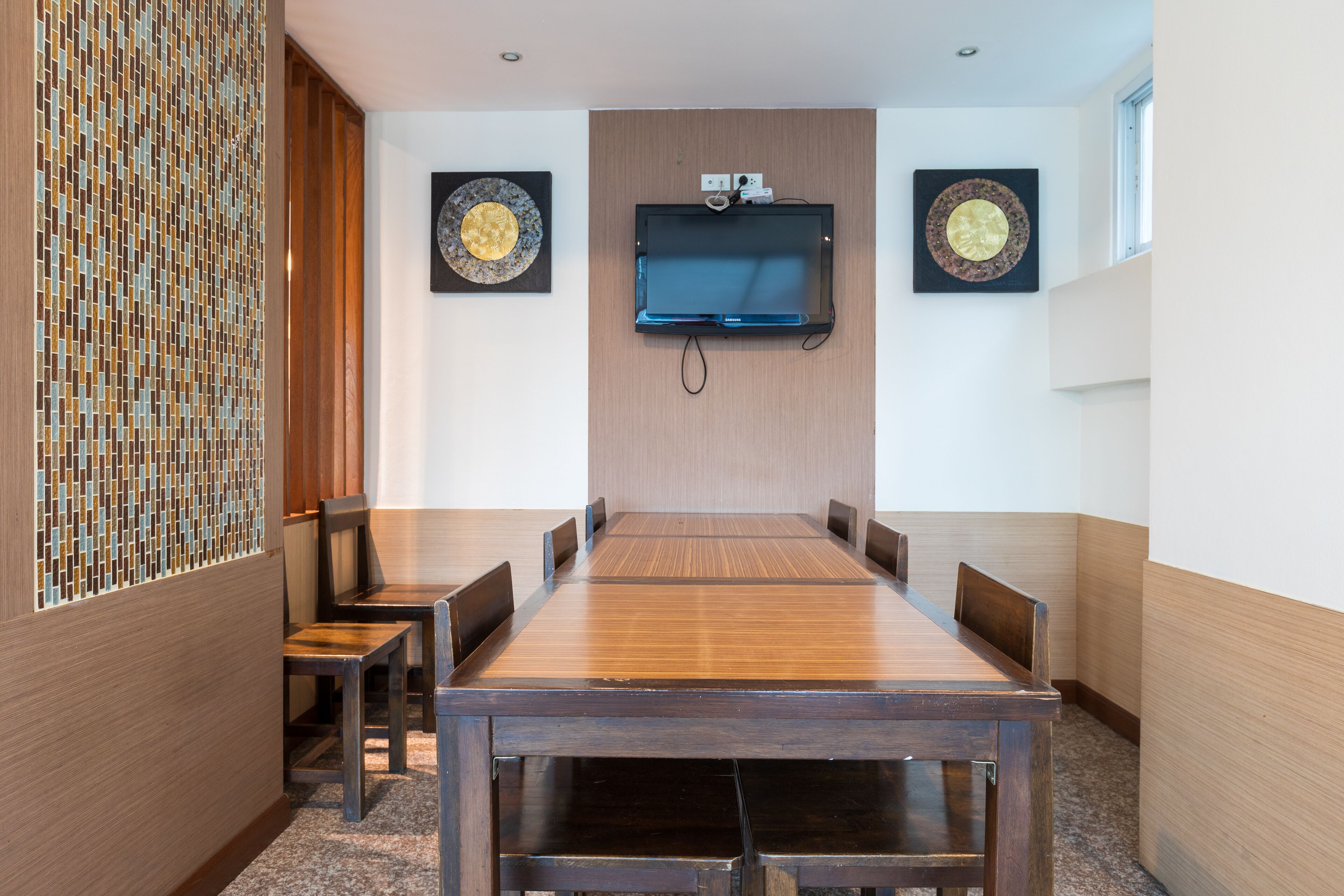 A conference room with a long wooden table, six chairs, two wall-mounted televisions, and decorative circular wall art.