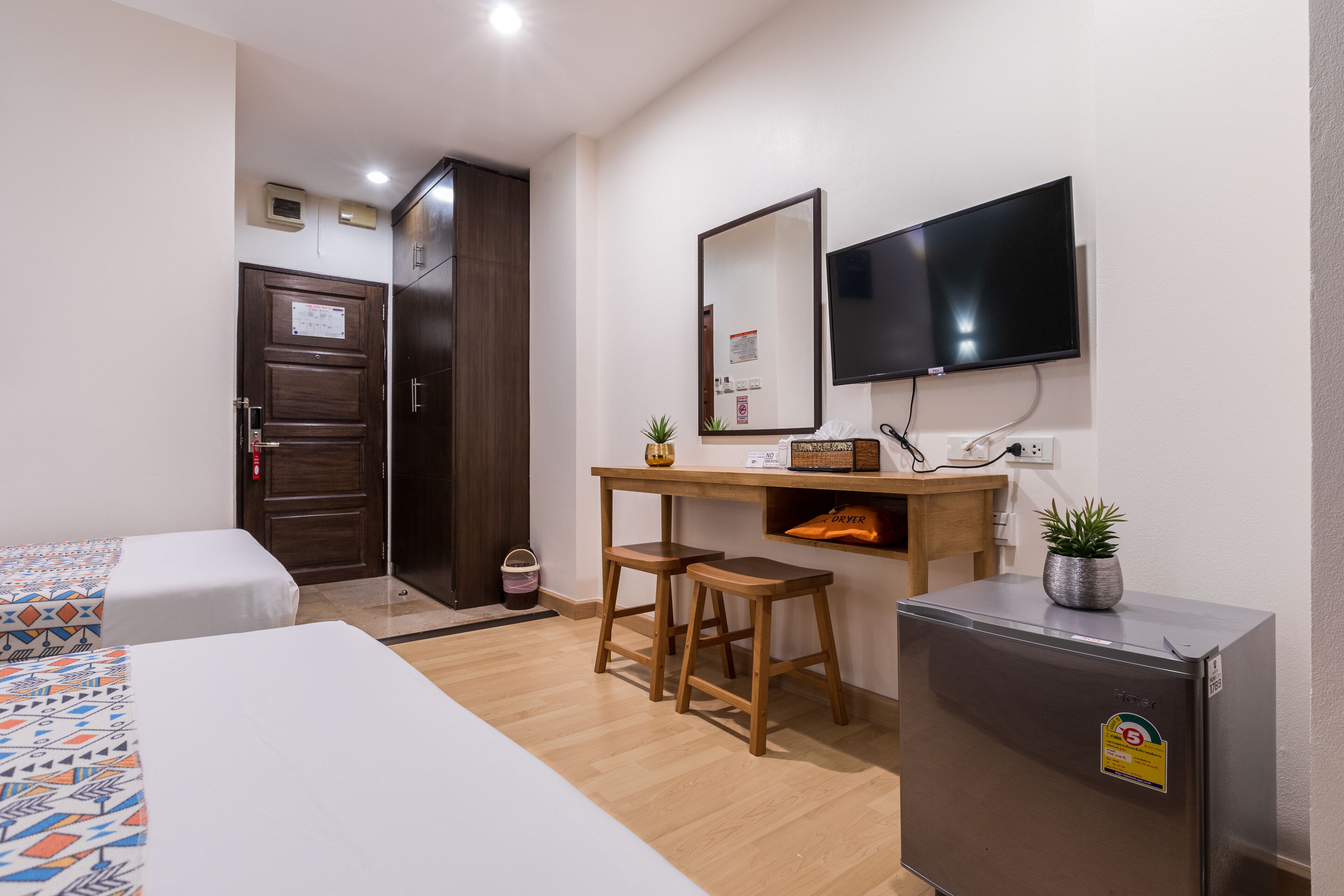 A hotel room with two beds, a desk with a chair, a TV, a small fridge, and a wooden door.