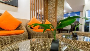 Ein modernes Wohnzimmer mit Rattanmöbeln, orangefarbenen Kissen und einem Glastisch mit Pflanze.