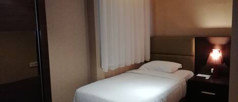 A neatly made bed in a hotel room with a headboard, a bedside table with a lamp, and a wall-mounted curtain.