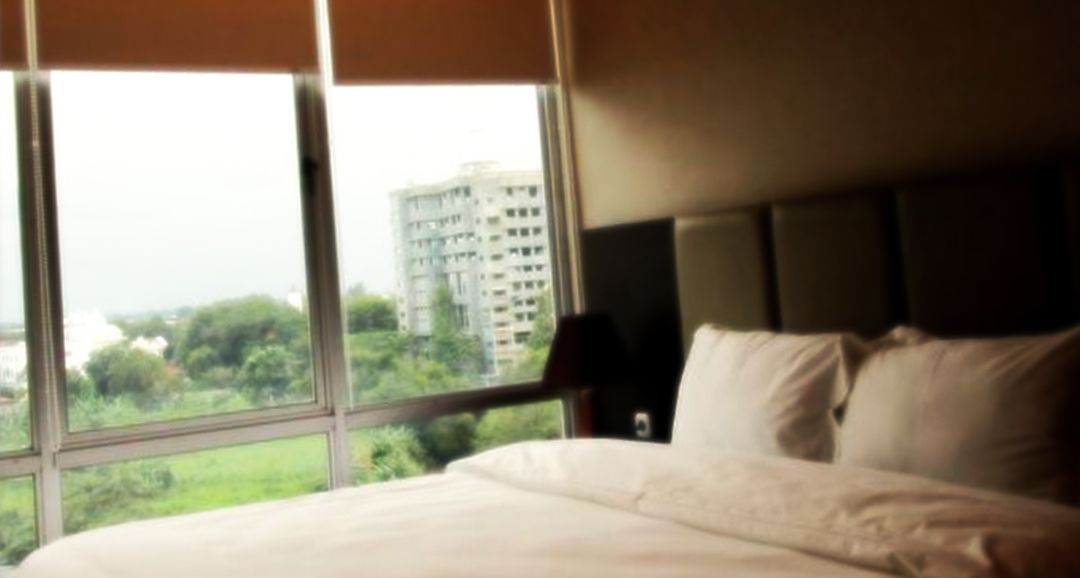A hotel room with a large window, a bed, and a nightstand.