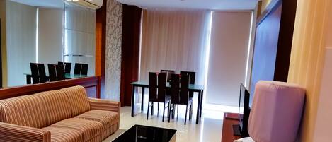 A modern living room with a sofa, a coffee table, a dining table with chairs, and a TV.
