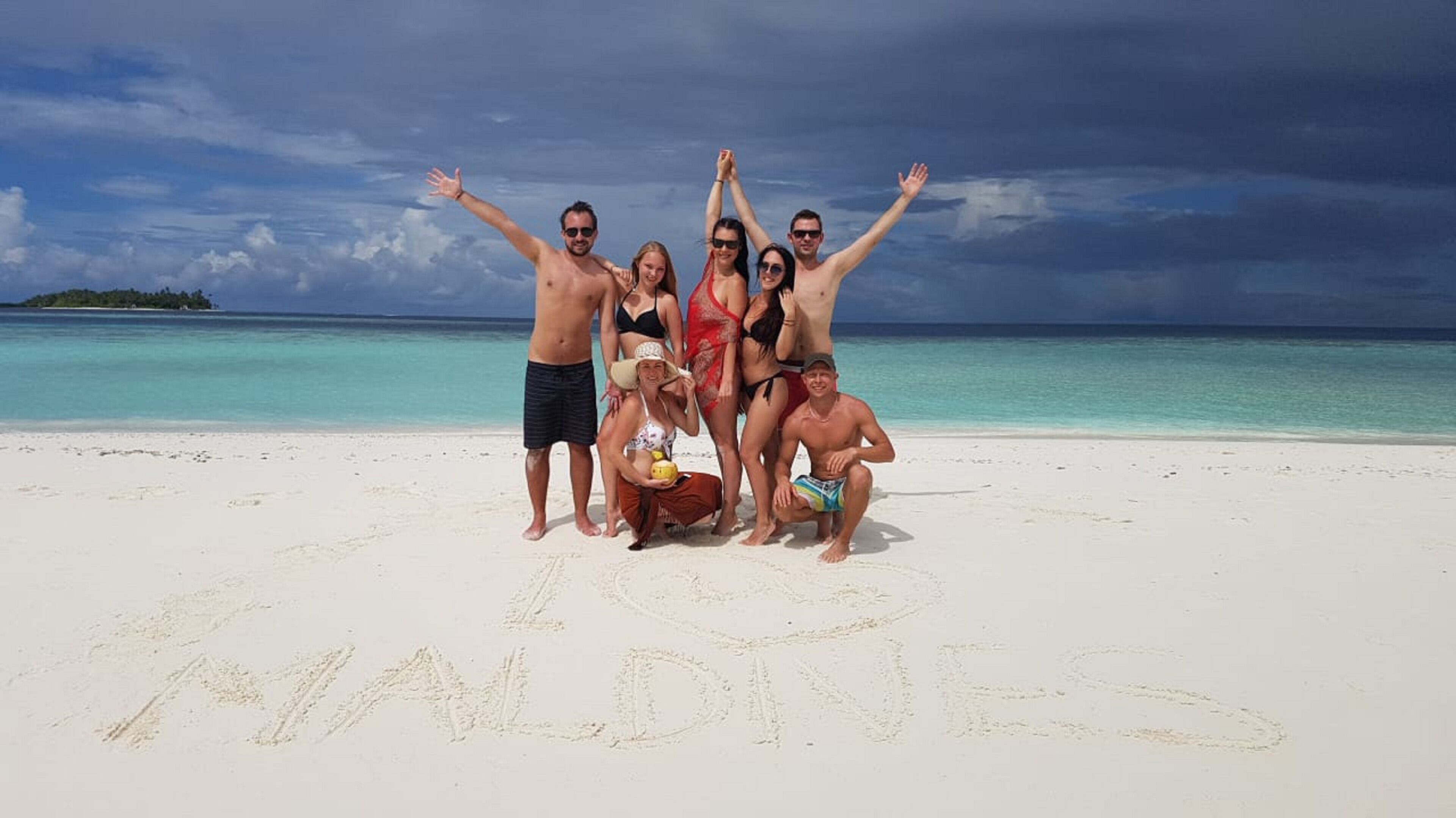 A group of people on a beach with the word "MALDIVES" written in the sand.
