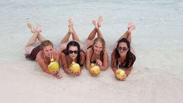 Four people lying on a sandy beach with their feet in the water, each holding a yellow drink.