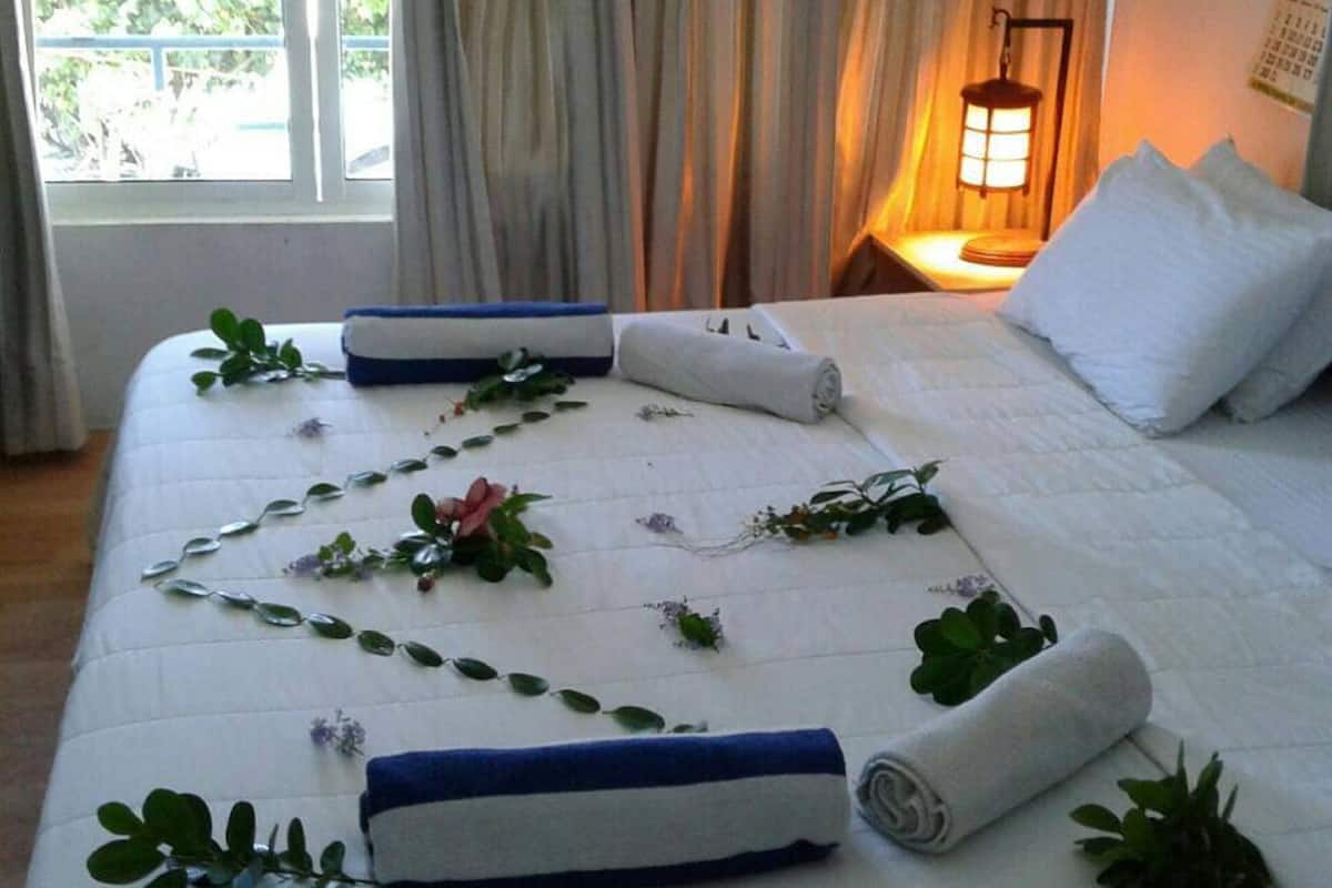 A neatly made bed with rolled towels, a decorative plant, and a bedside lamp in a room with a window and curtains.
