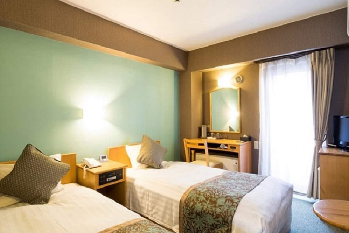 A hotel room with two beds, a desk, a mirror, and a television.