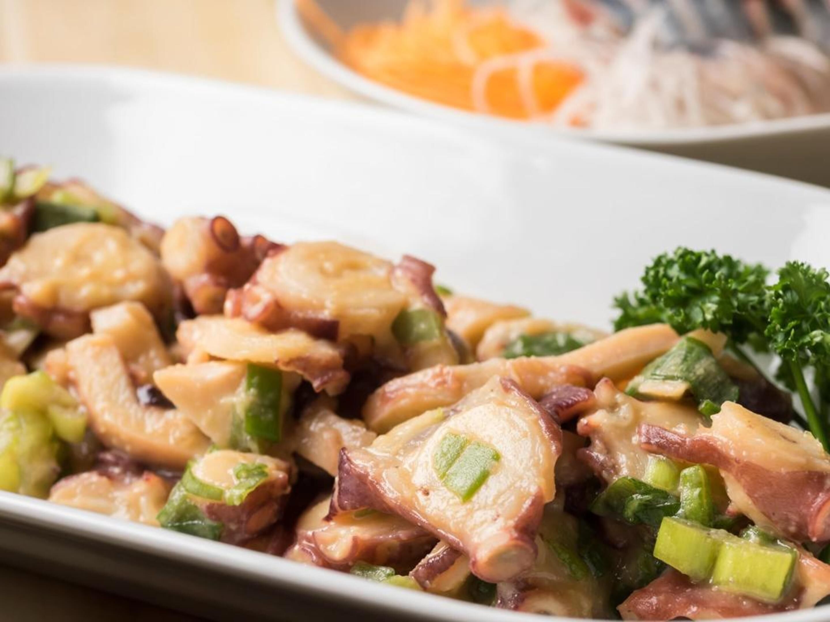 A dish with octopus, green vegetables, and possibly bacon, served on a white plate.