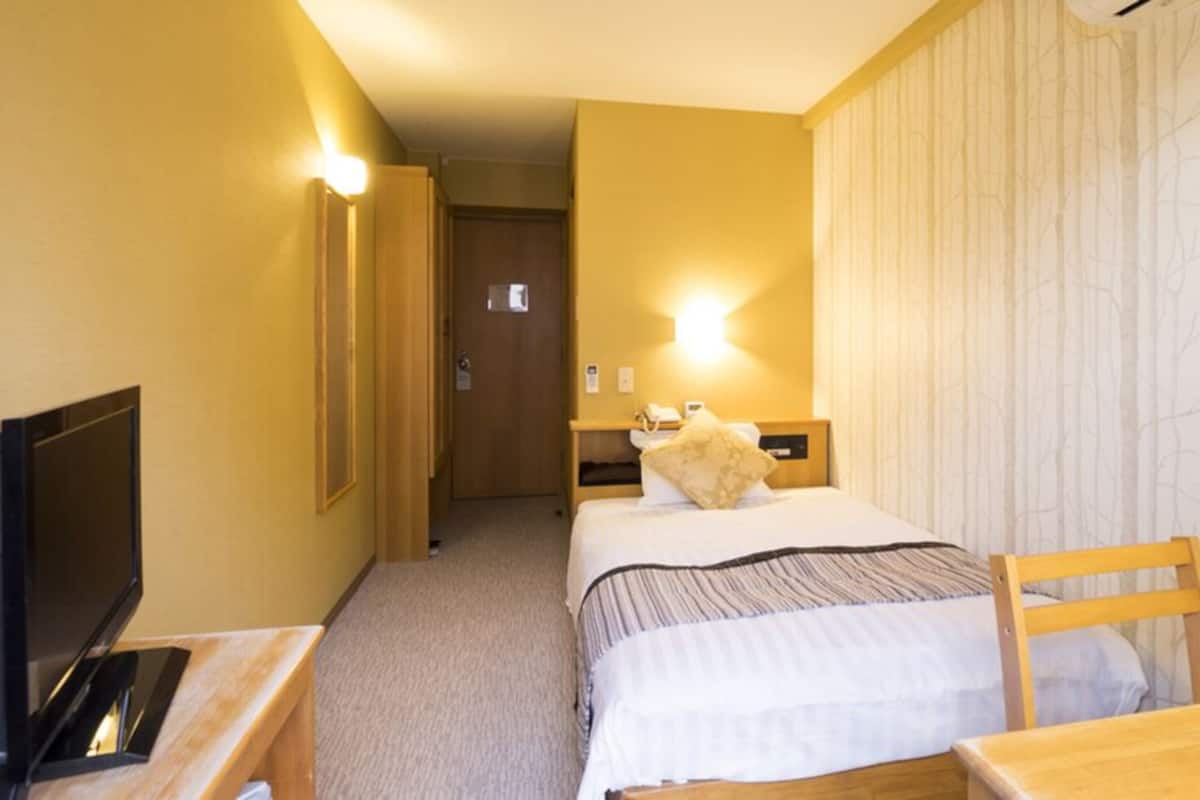A hotel room with a bed, bedside tables, a television, and a door leading to a hallway.