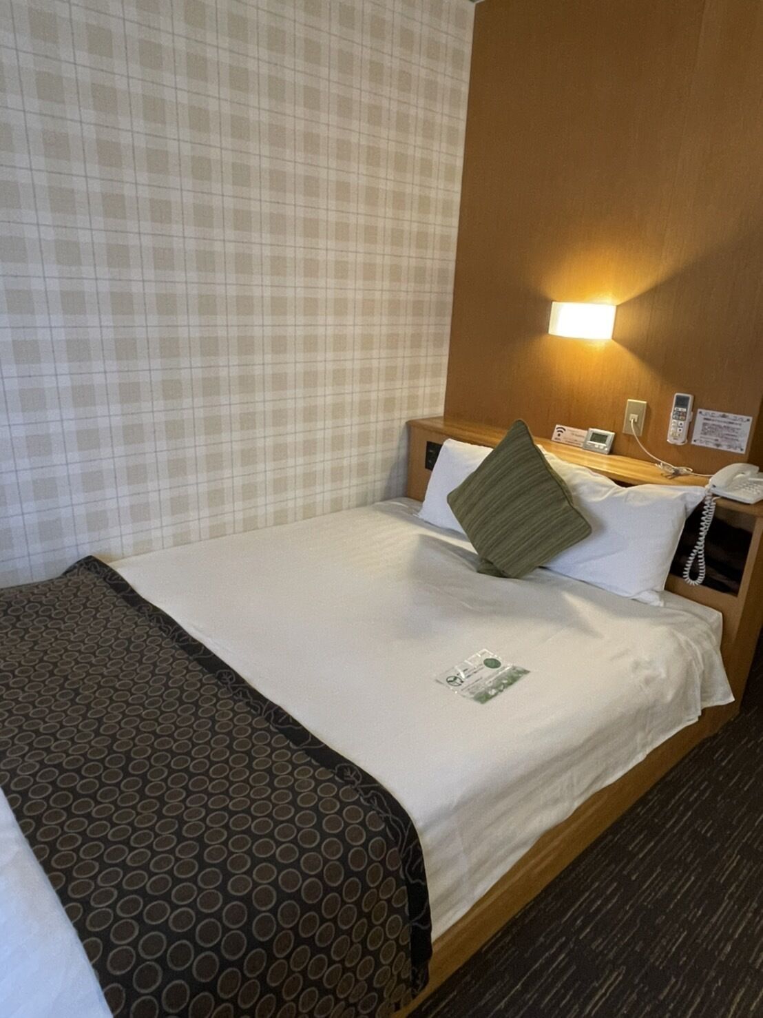 A hotel room with a bed, a nightstand, a phone, and a wall-mounted light.
