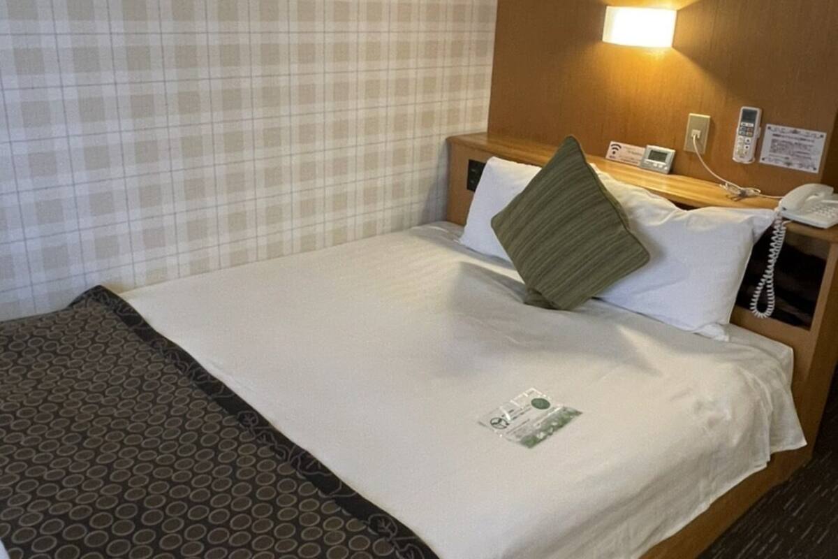 A hotel room with a bed, a nightstand, a phone, and a wall-mounted light.