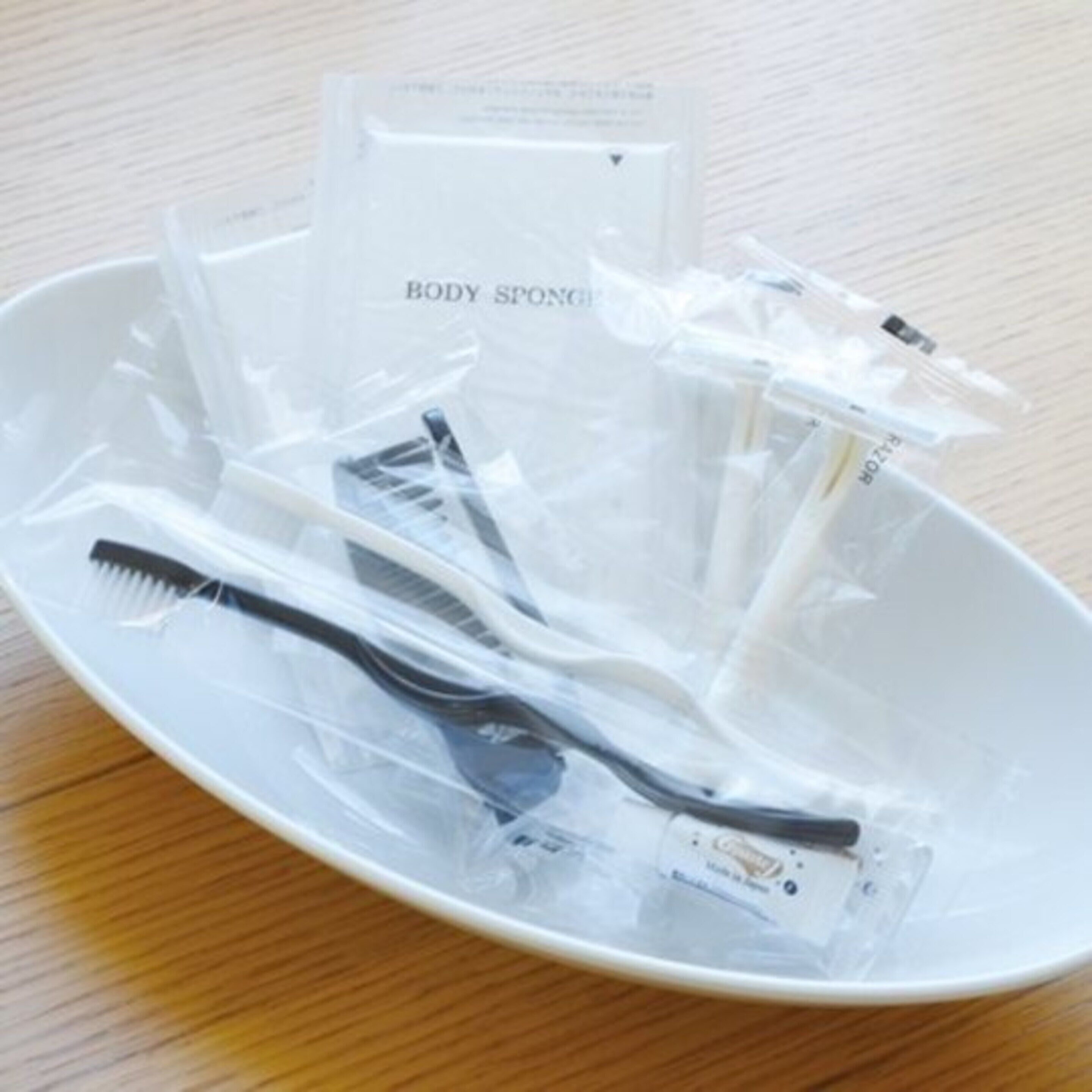 Ein weißer Teller mit verschiedenen Pflegeartikeln wie Zahnbürsten und Badeschwämmen, alles in transparenter Kunststoffverpackung.