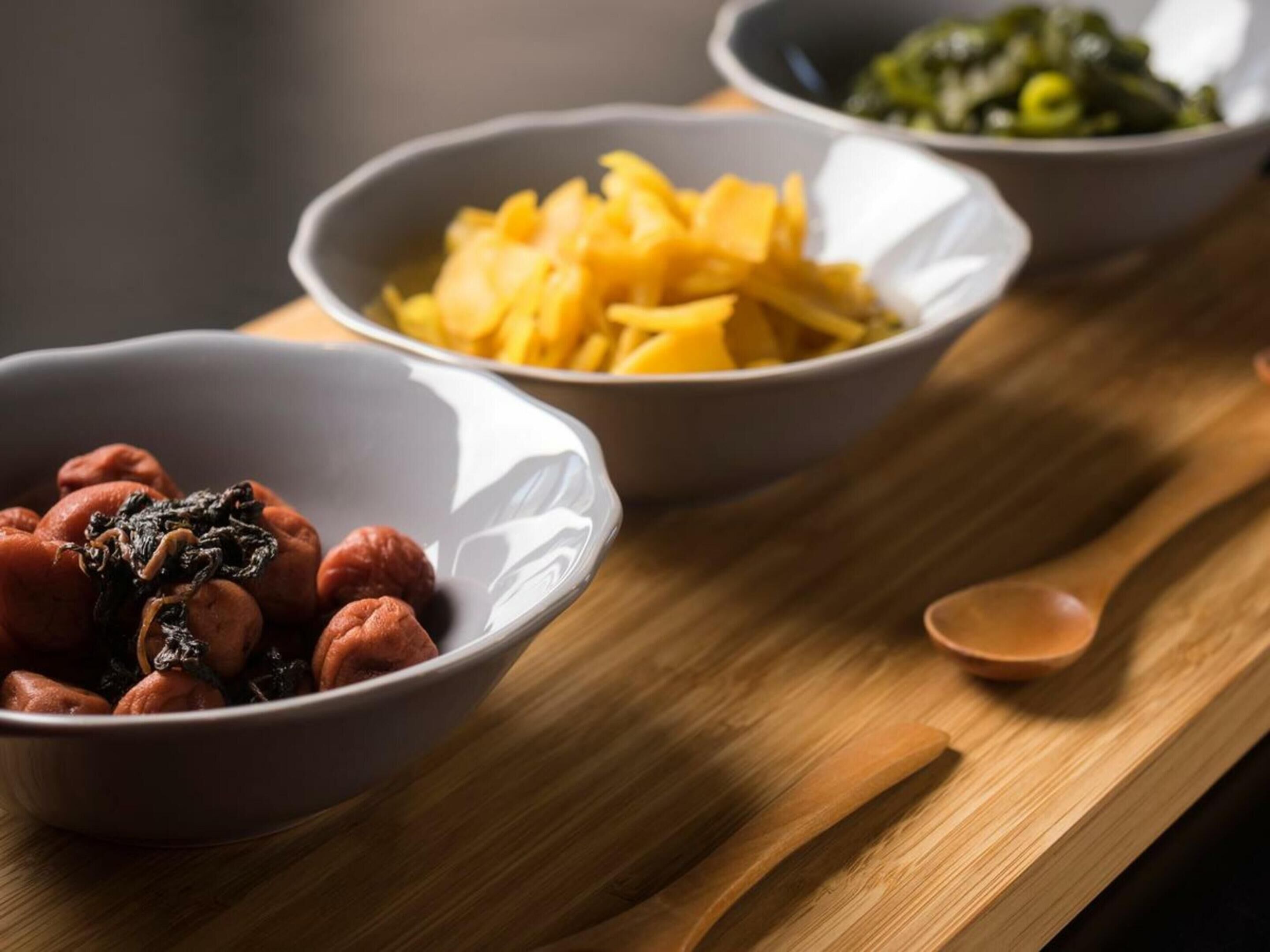 Three bowls of food on a wooden table.