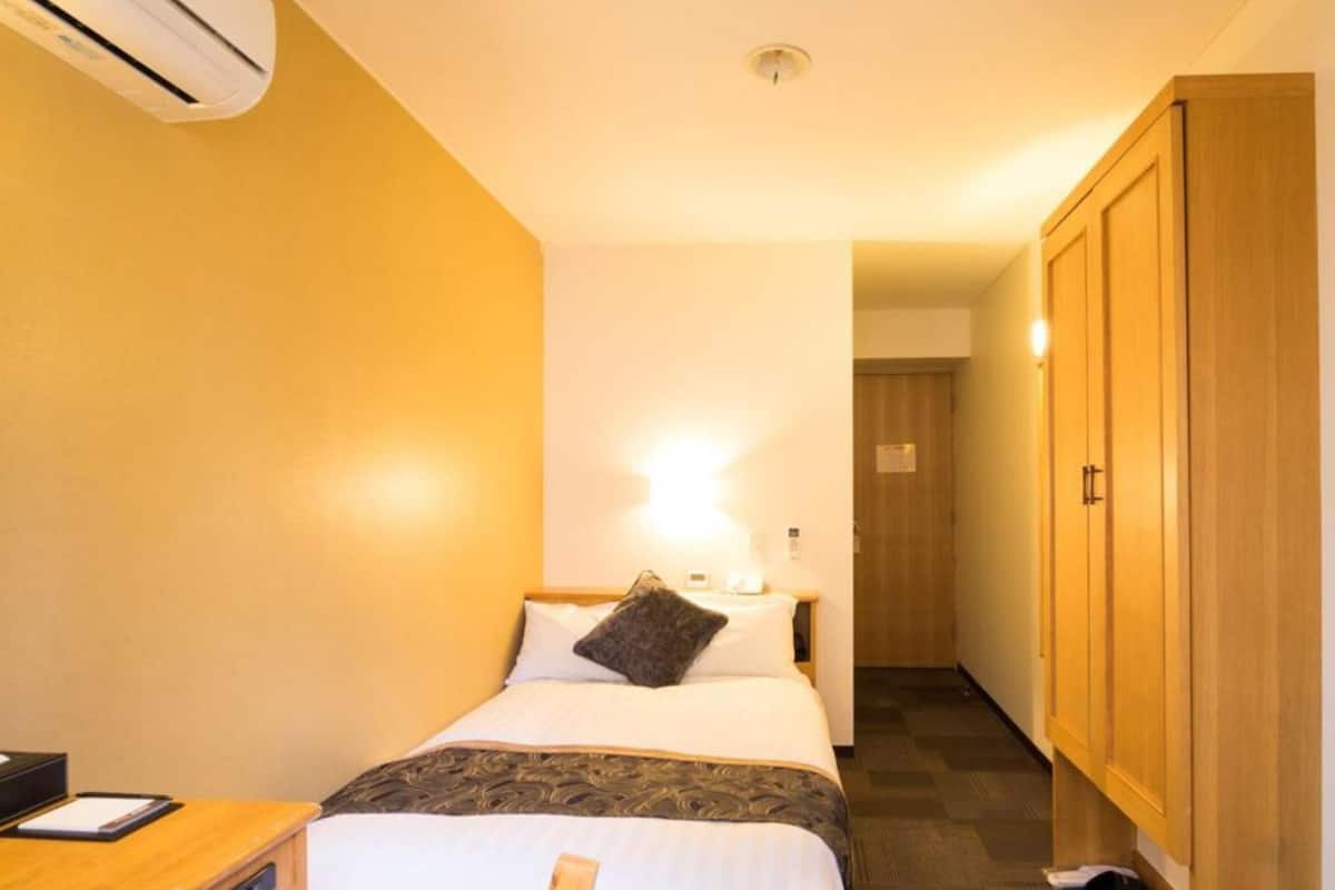 A small, neatly arranged hotel room with a bed, bedside table, and a wardrobe.