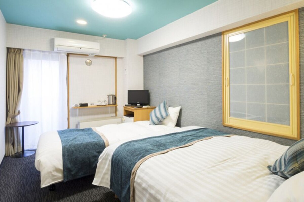 A hotel room with two beds, a television, a small table, and a window.