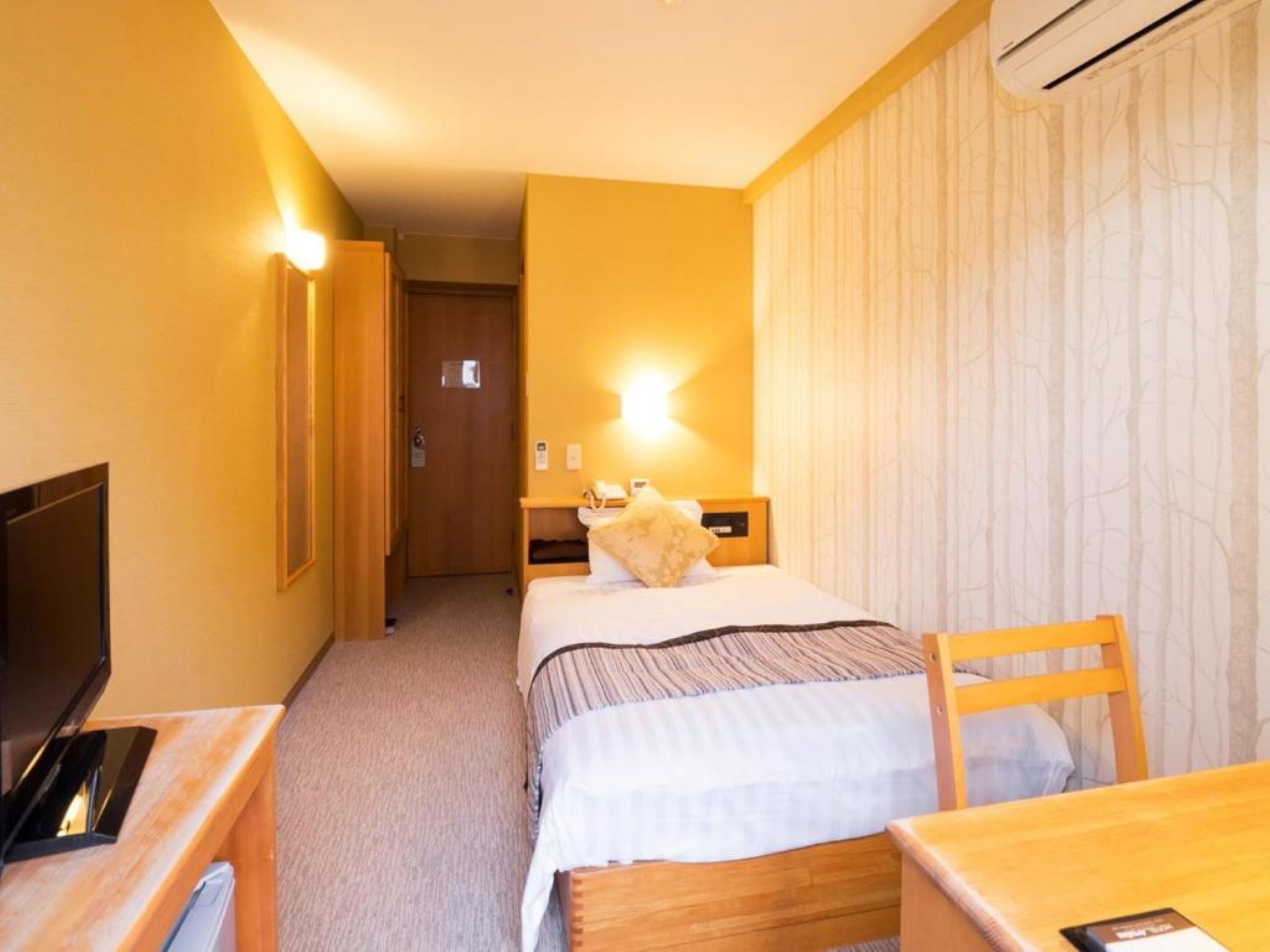 Een hotelkamer met een bed, nachtkastje, stoel, bureau en een televisie.