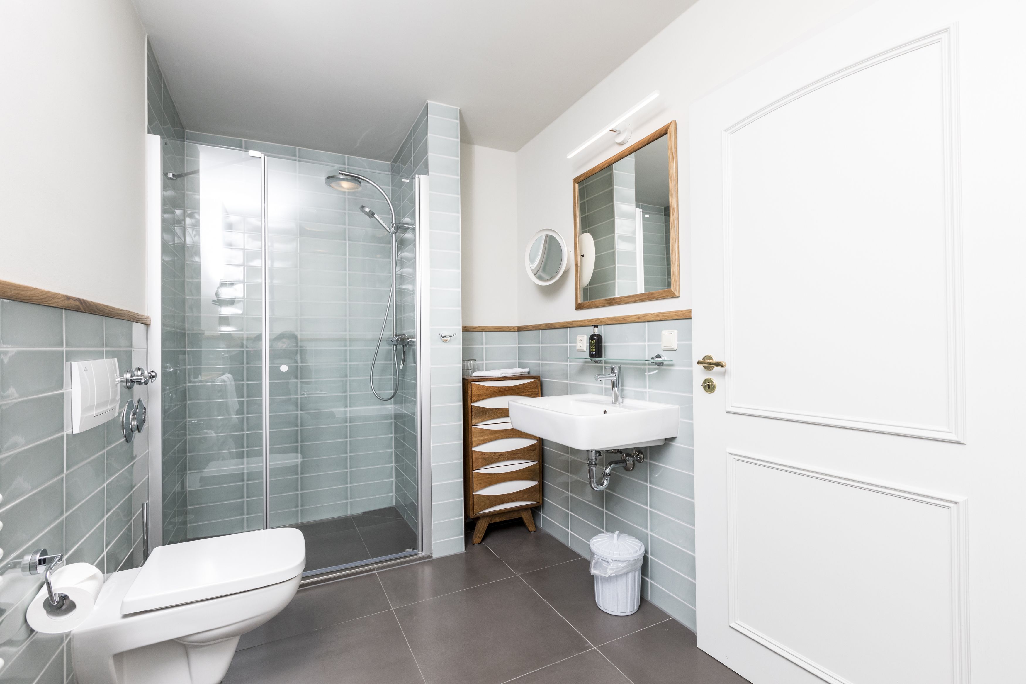 Een moderne badkamer met een douchecabine van glas, een wit wastafel en een houten opbergmeubel.
