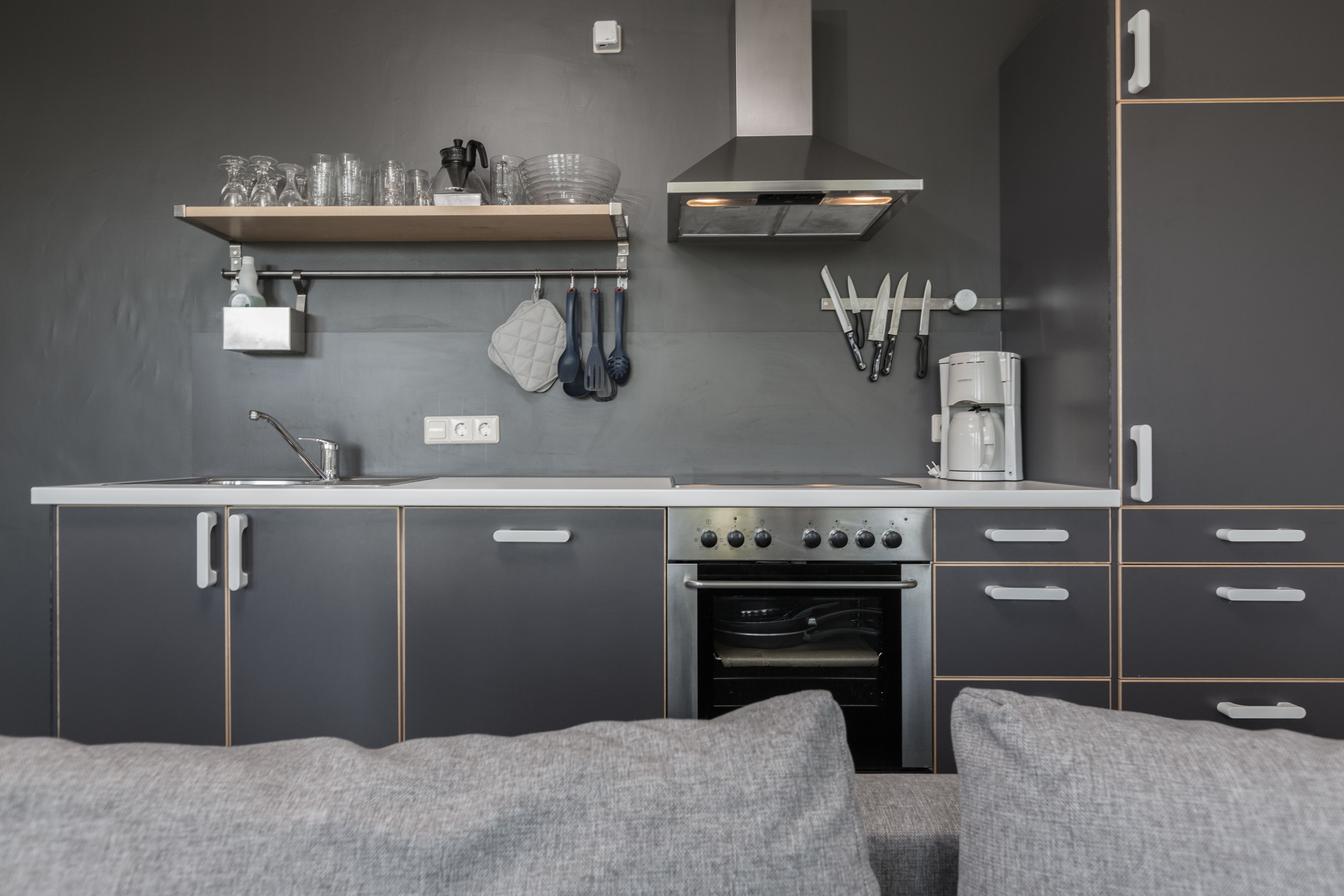 A modern kitchen with grey cabinets, a stainless steel range hood, and a built-in oven.