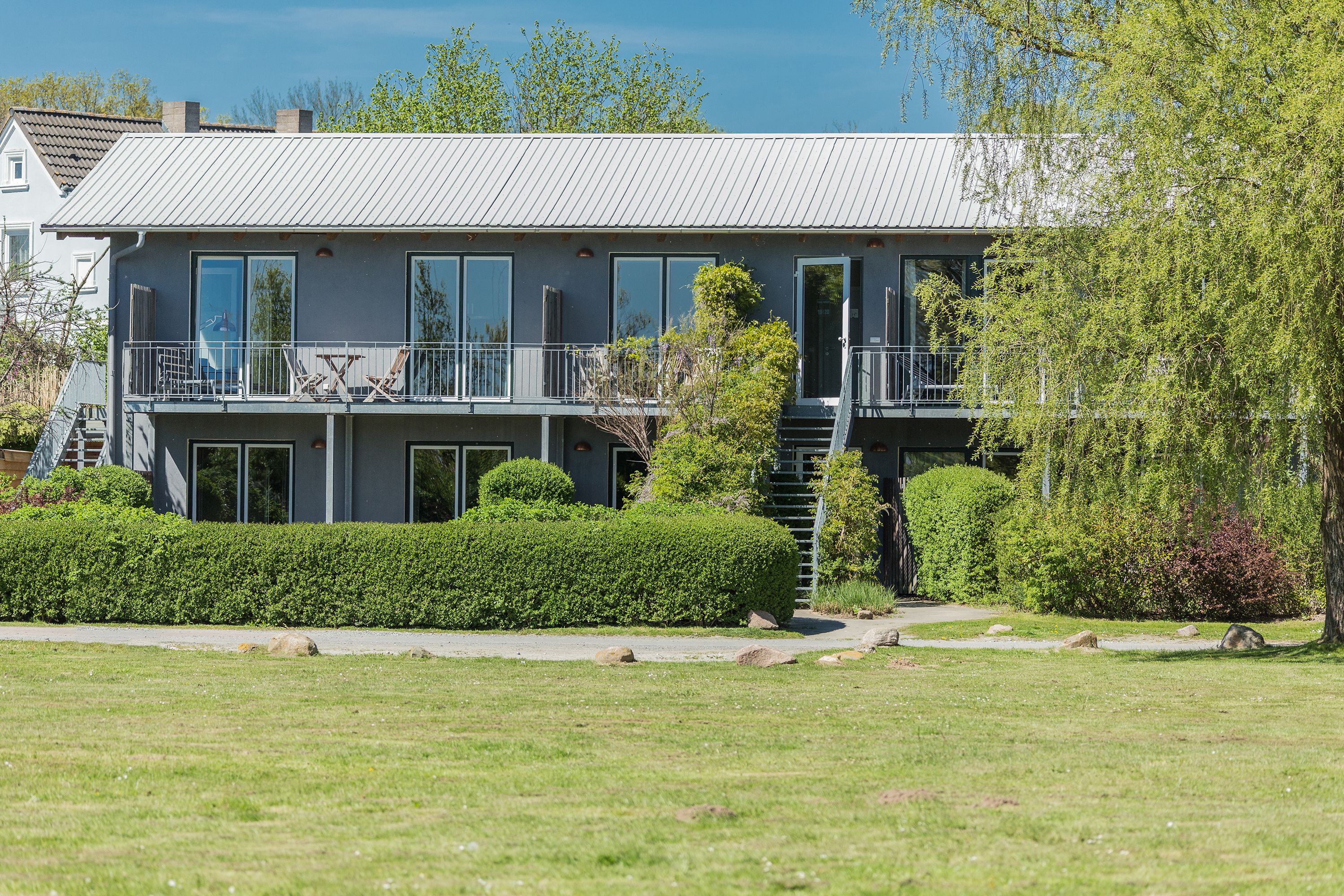 A modern two-story house with a balcony, large windows, and a well-maintained lawn.