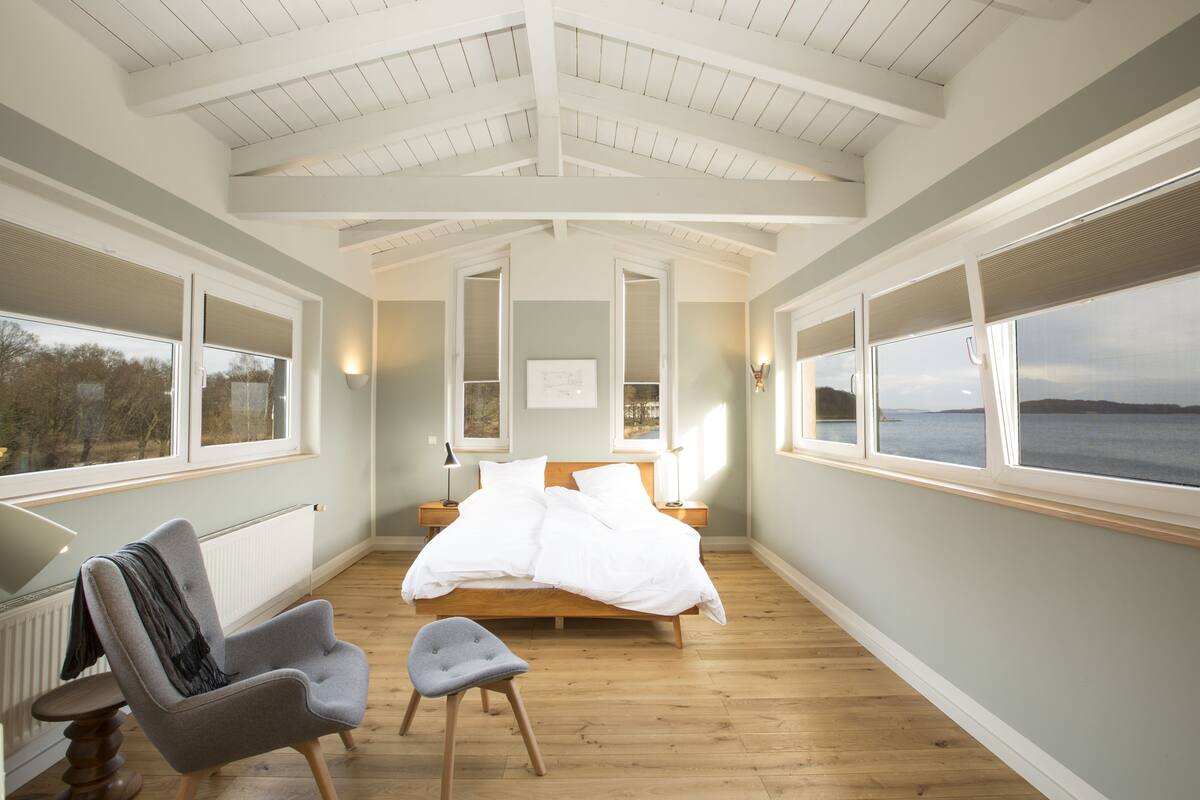 A bedroom with a large bed, a chair, and a view of the sea.