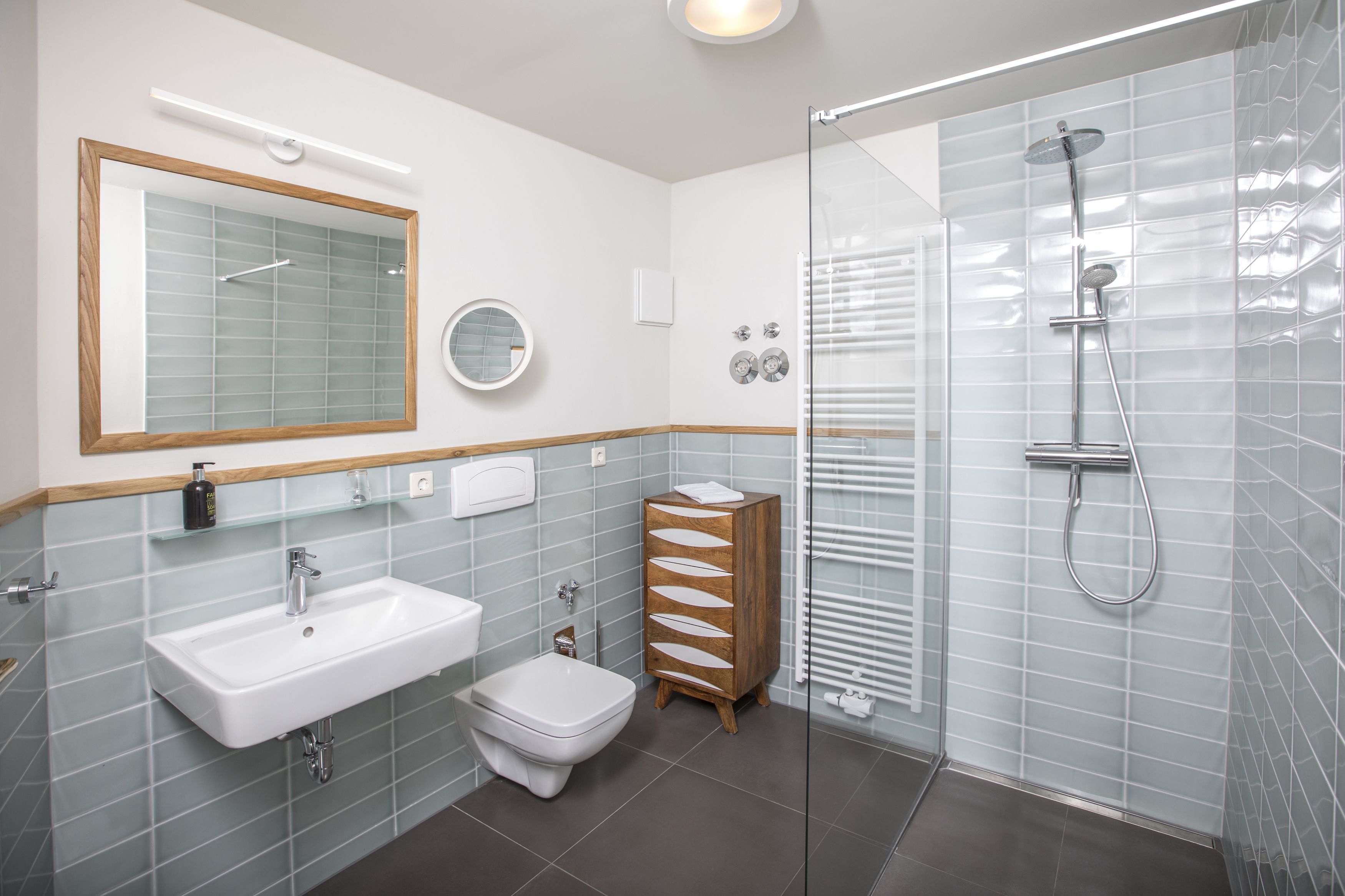 A modern bathroom with a glass shower enclosure, a white sink, a bidet, and a wooden vanity.