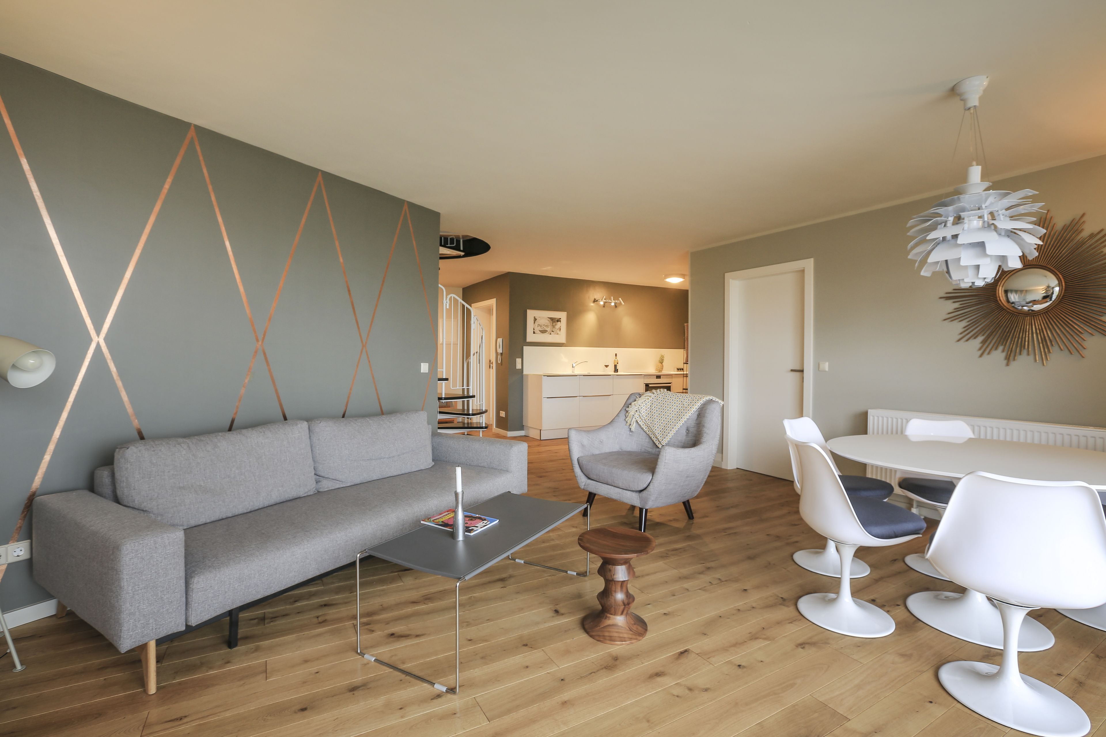 A modern living room with a grey sofa, a coffee table, and a dining area with white chairs and a table.