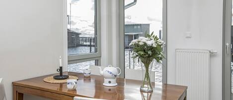 A dining area with a wooden table, white chairs, a vase with flowers, a white teapot, and a candle.