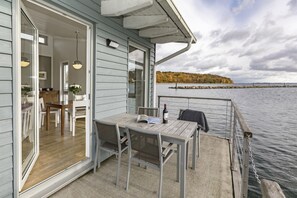 A wooden deck with a table and chairs, a dining area with a table and chairs, and a view of a lake with a dock. - Im-Jaich Wasserferienwelt (Putbus)