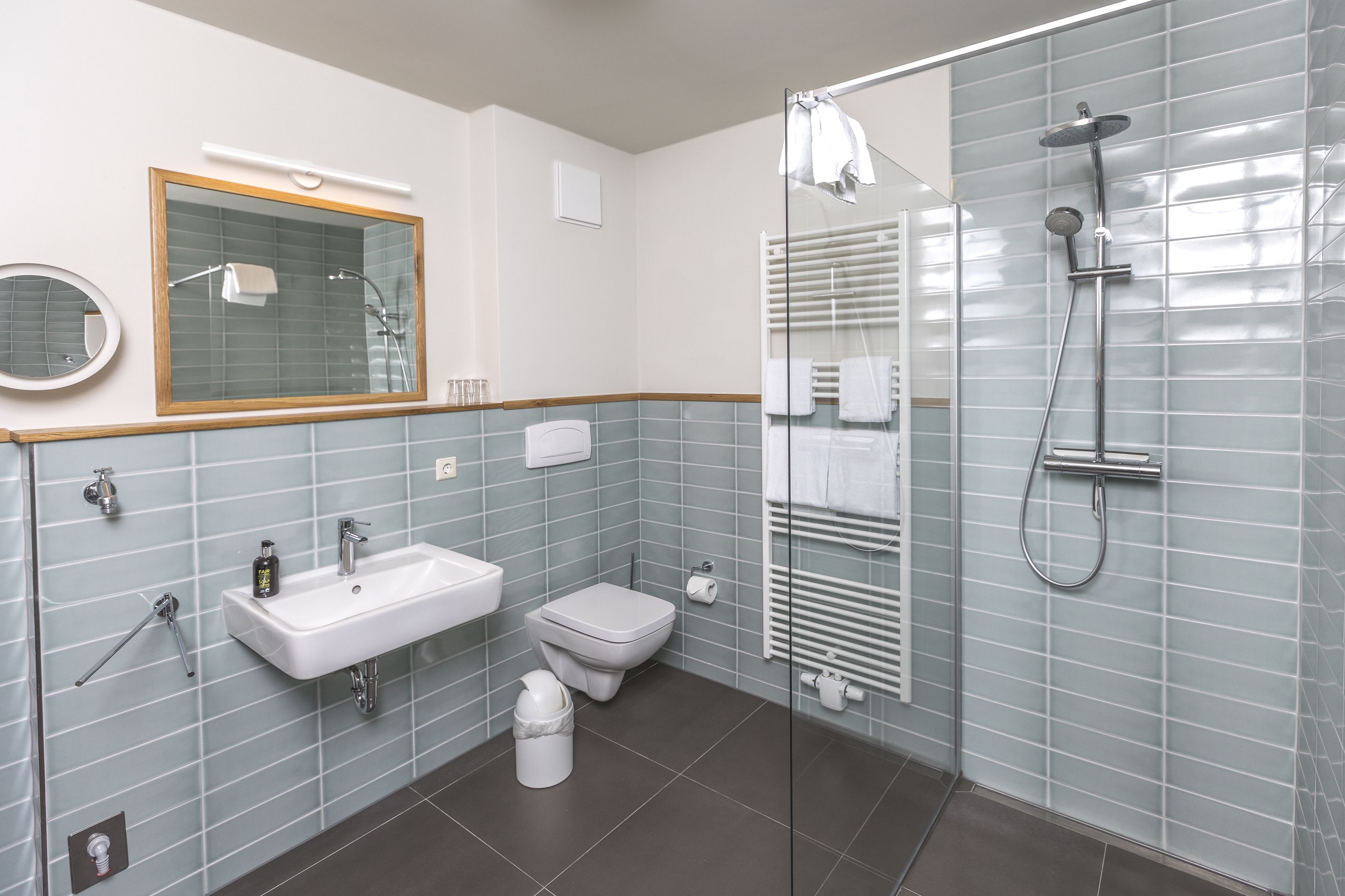 Ein modernes Badezimmer mit einer Duschkabine aus Glas, einem Waschbecken, einer Toilette und einem Spiegel.