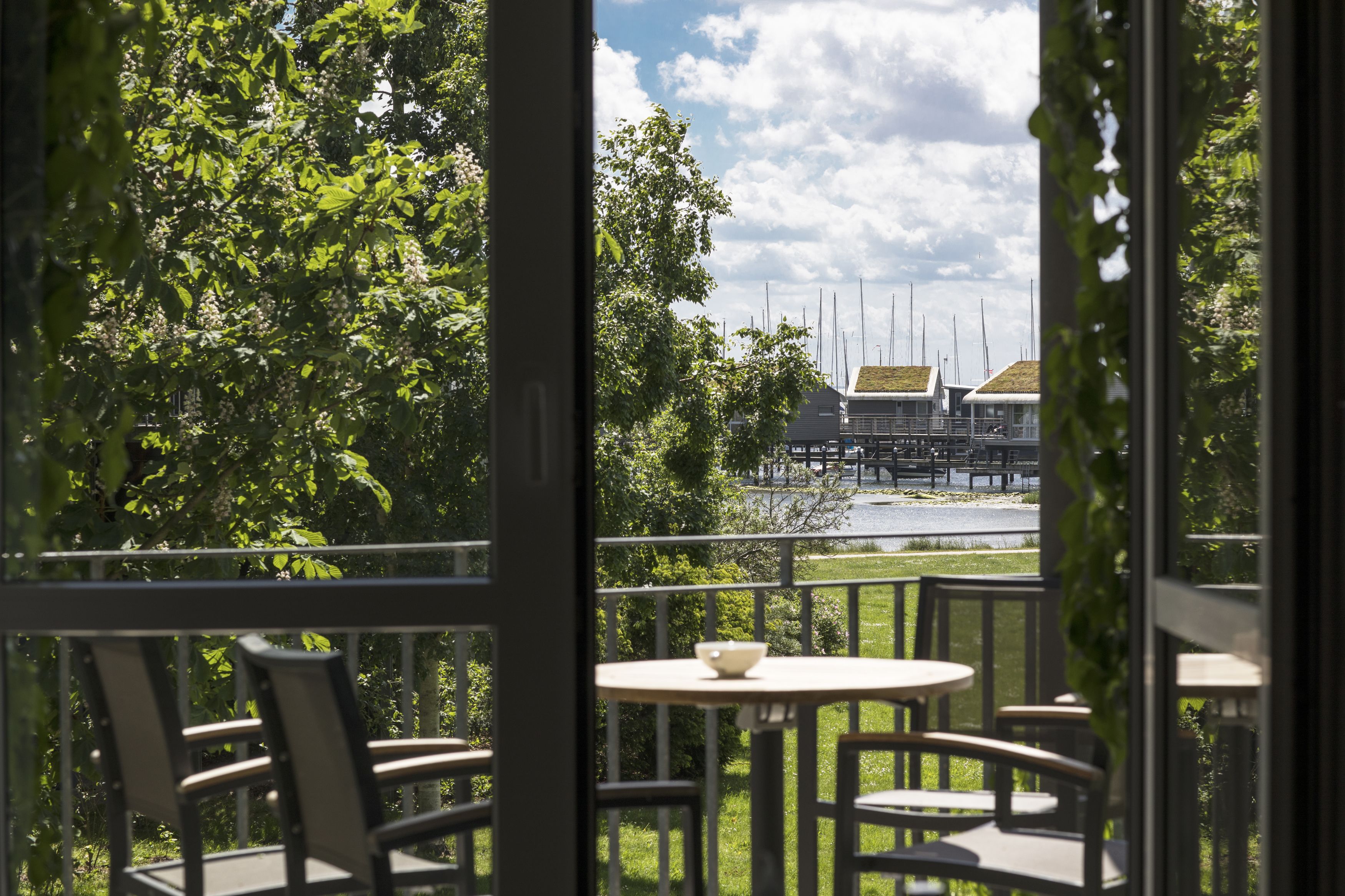 Een balkon met stoelen en een tafel, met uitzicht op een tuin en een gebouw met een groen dak.