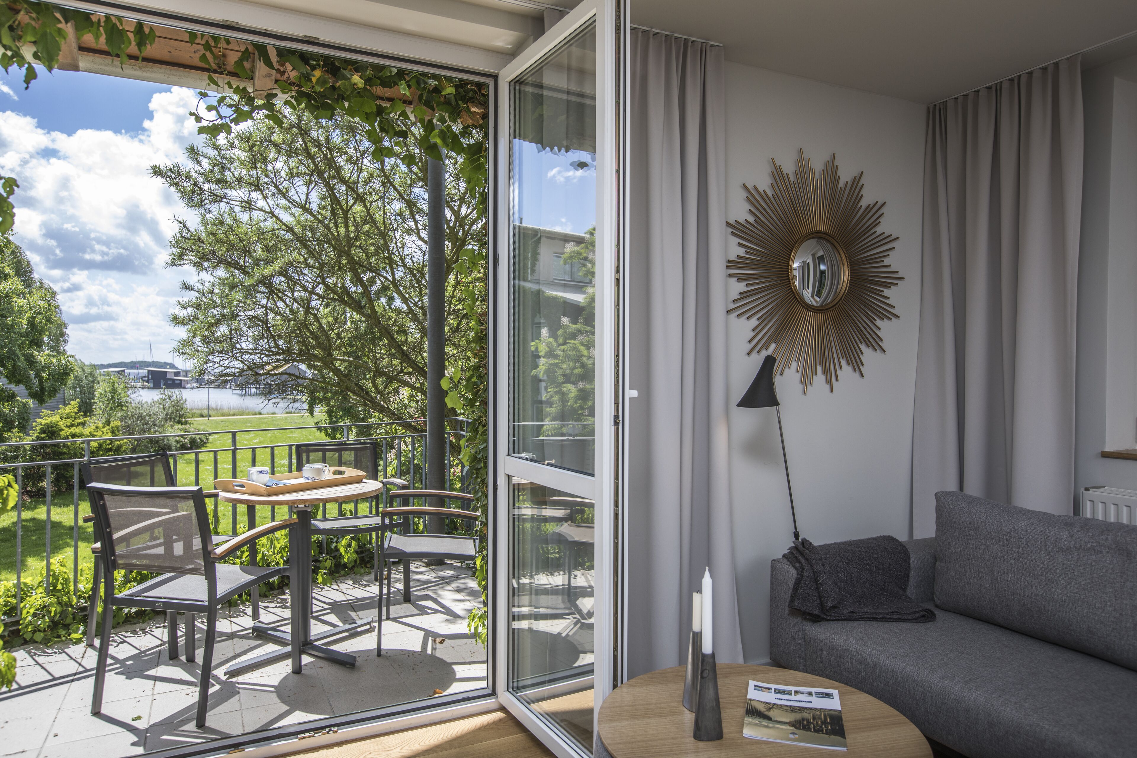 Una sala de estar moderna con balcón, un sofá, una mesa de comedor con sillas y un espejo decorativo.
