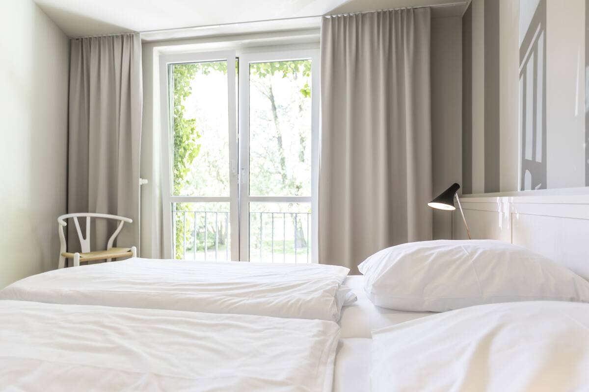 A bedroom with two beds, a chair, a desk, and a window with curtains.