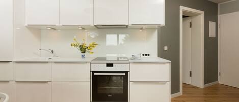 A modern kitchen with white cabinetry, a built-in oven, and a small countertop with a vase of flowers.