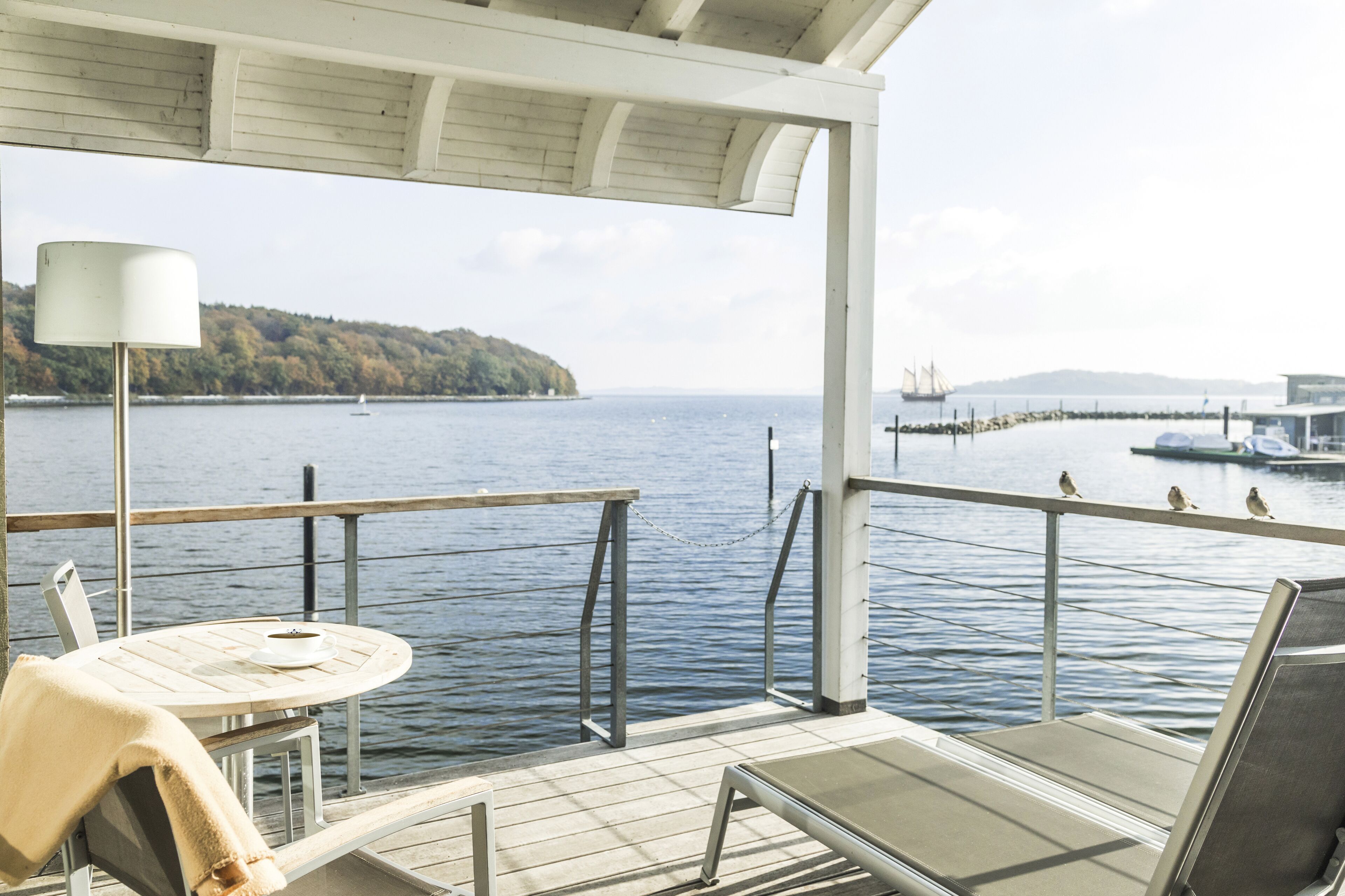 Terraza con mesa y sillas, con vista a un cuerpo de agua y una isla distante con un muelle.