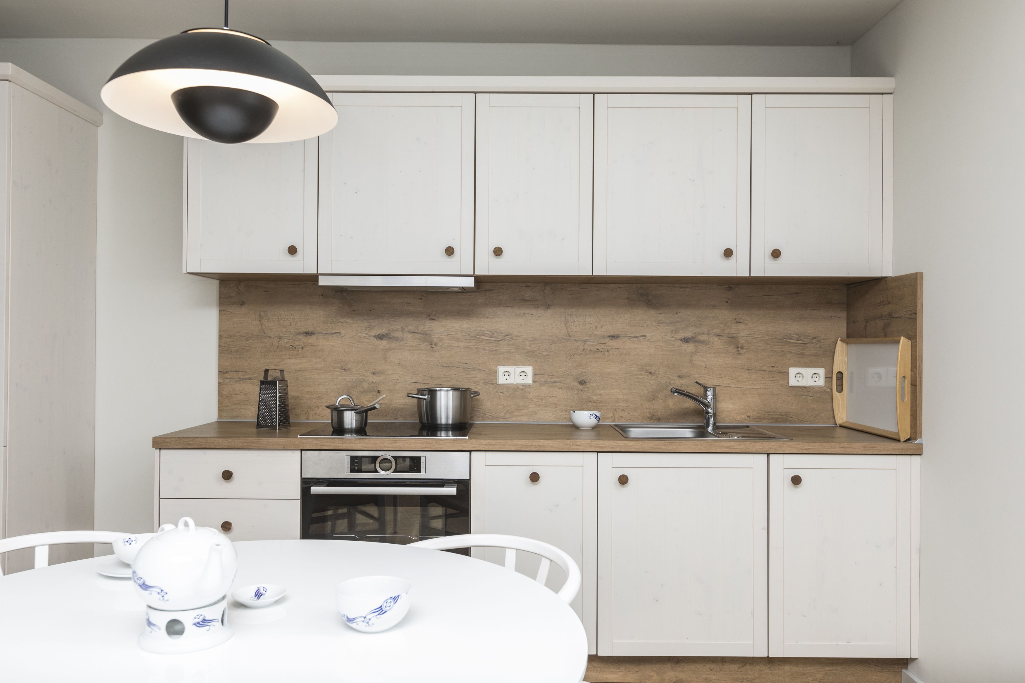 A modern kitchen with white cabinets, a wooden countertop, a built-in oven, and a dining area with a white table and chairs.