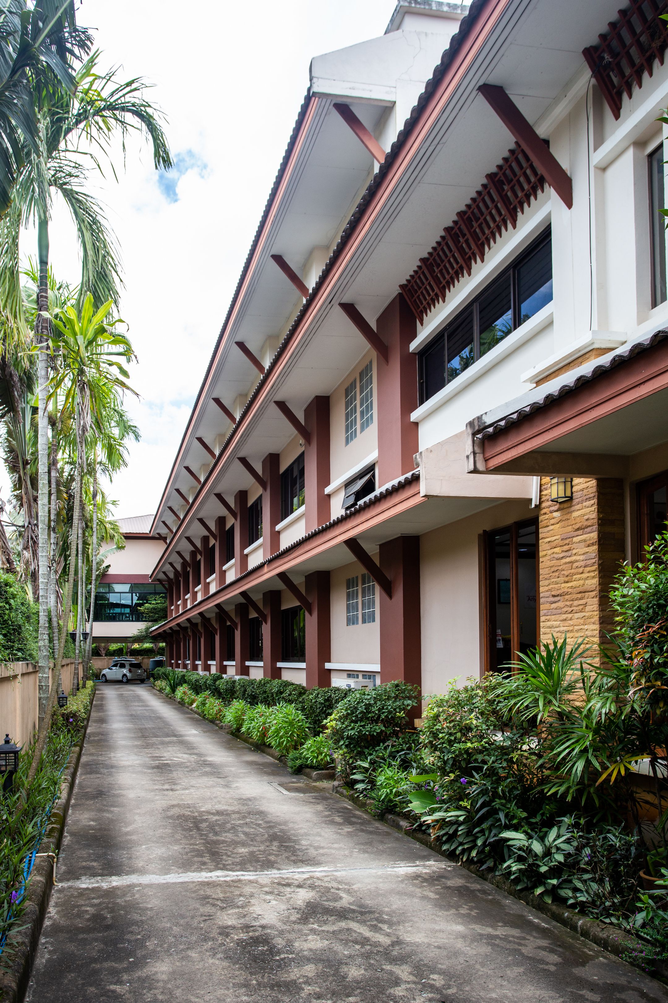 A row of hotel rooms with a central corridor, surrounded by lush greenery and palm trees.