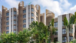 Un hotel moderno con varios pisos, un llamativo letrero LE GROVE y exuberantes plantas tropicales en primer plano.
