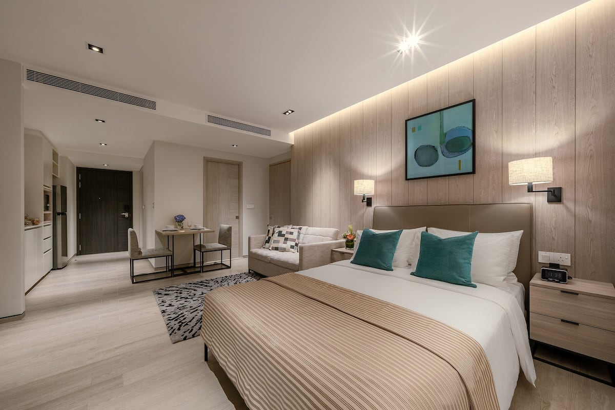 Habitación de hotel moderna con una cama grande, un escritorio y una silla. Hay una mesita con un jarrón de flores y una lámpara en la pared.