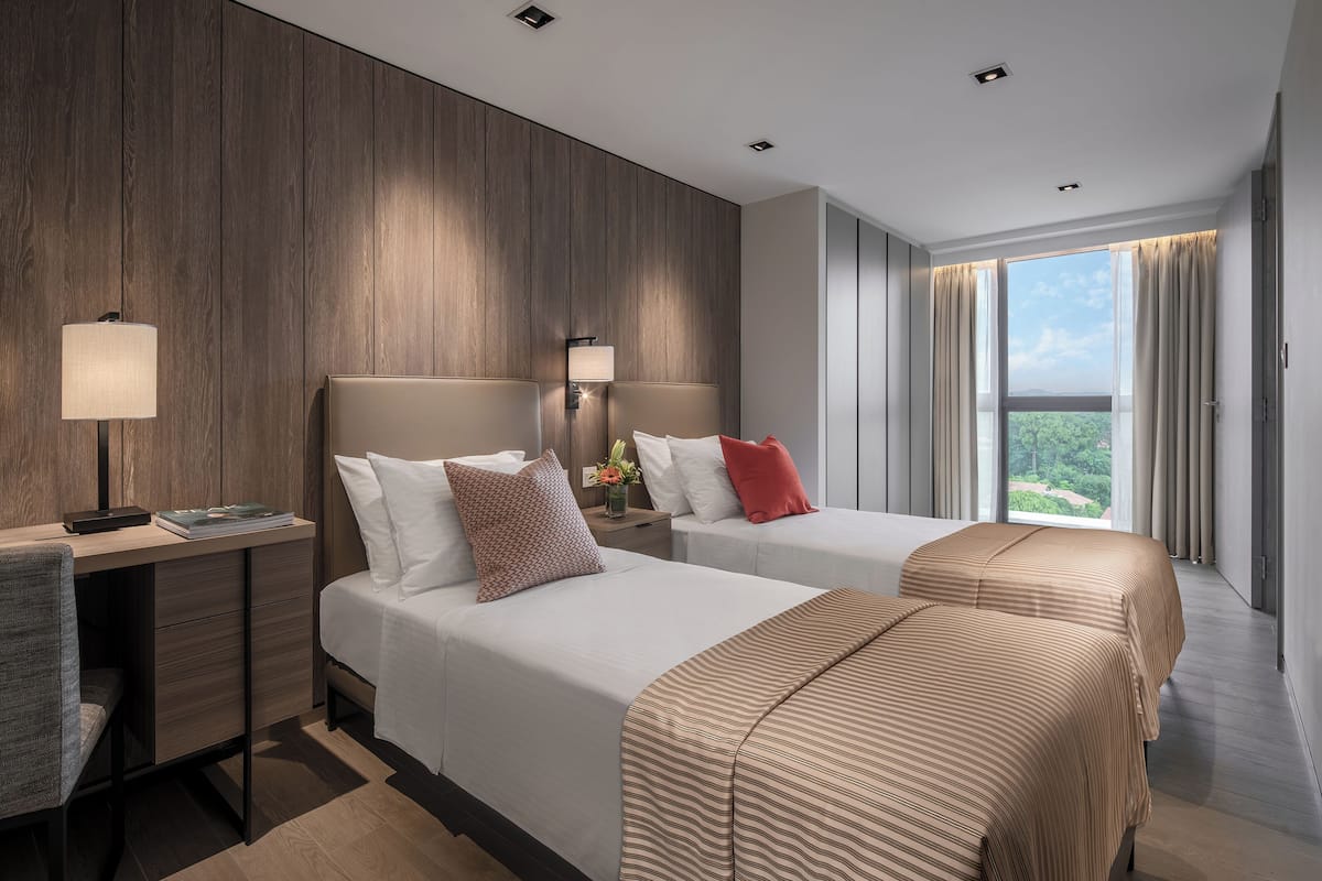 Habitación de hotel con dos camas, un escritorio y vista a zonas verdes.