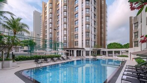 Un hotel moderno con piscina, sillas de descanso y vistas a edificios altos.