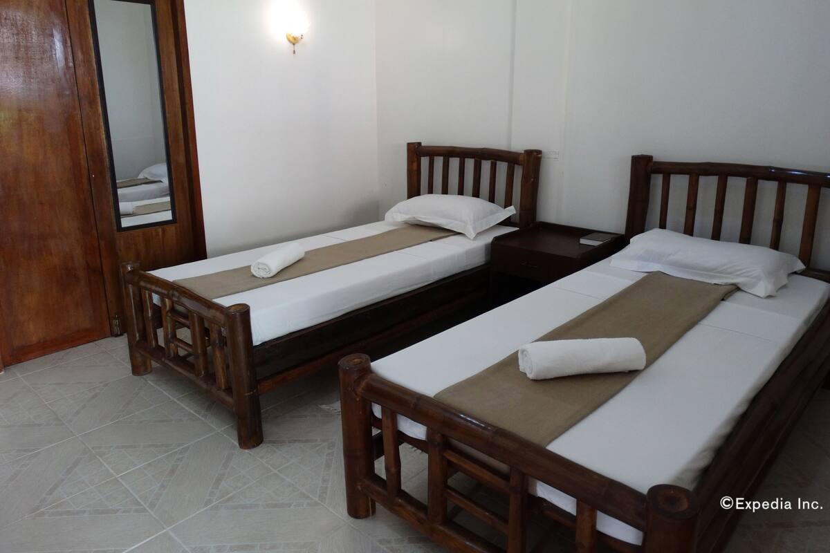 Habitación doble con dos camas de madera, una mesita de noche pequeña, un velador y un espejo, además de suelo de baldosas.