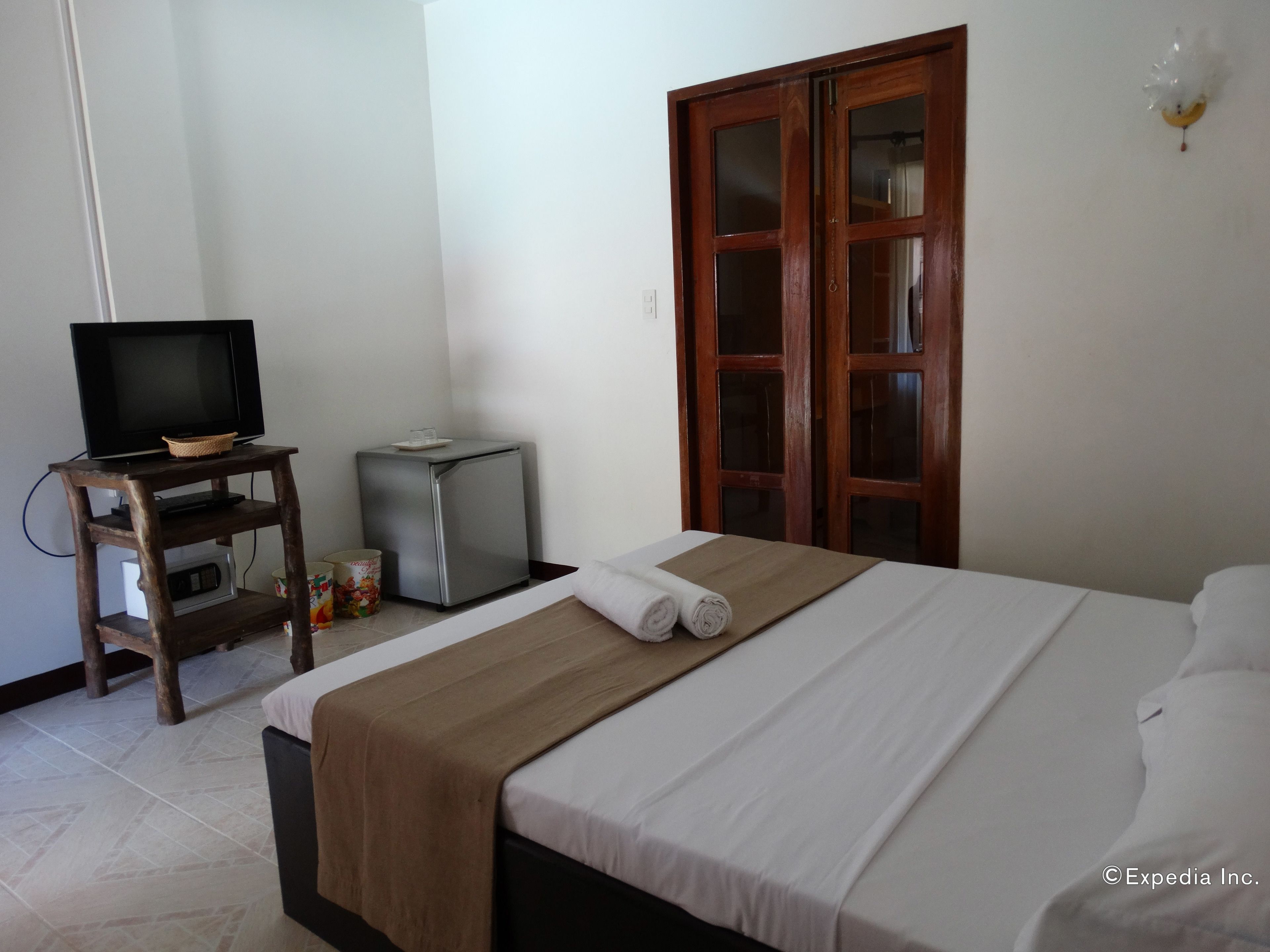 A hotel room with a bed, a TV on a wooden stand, a small fridge, and a wardrobe.