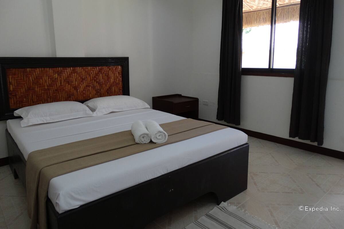 Una habitación de hotel con una cama, una mesita de noche y una ventana con cortinas.