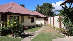 Ein eingeschossiges Haus mit rotem Dach, beige farbenen Wänden und einem kleinen Vorgarten mit einem Weg zum Eingang.